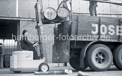 Der Fahrer des Gabelstaplers "Muli" hebt mit der Gabel des Flurfördergeräts zwei Tonnen auf die Ladefläche des Lastwagens am Togokai des Südwesthafens. Zwei Arbeiter verladen die Tonnen auf dem Lastkraftwagen; ca. 1952.