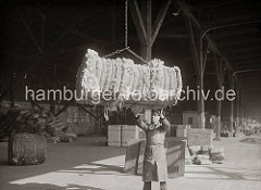 Ein Wollballen hängt im Ladegeschirr und wird von einem Hafenarbeiter am Kai angenommen. Im Hintergrund sind in dem offenen Schuppen Kisten und Säcke gelagert, ca. 1934.