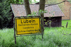 Ortsschild Lübeln, Gemeinde Küsten / Landkreis Lüchow-Dannenberg. Im Hintergrund ein Holzstall auf einer Wiese.