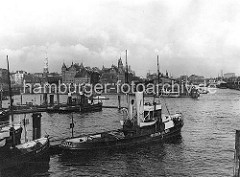 Schlepper an ihrem Liegeplatz am Baumwall; im Hintergrund die Speicherblöcke J + K, die zu beiden Seiten des Kehrwiederfleet legen. Rechts die Einfahrt zum Sandtorhafen - Frachtdampfer liegen am Kaiserkai. Am Sandtorhöft hat eine Hafenfähre an