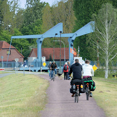 Fahrradfahrer und Spaziergänger auf dem Deich am Dömitzer Hafen - im Hintergrund die Klappbrücke über den Müritz Elde Kanal.
