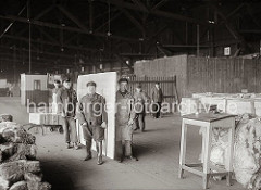 Mit Handhaken haben die Arbeiter die schwere Marmorplatte aufgenommen und tragen diese an ihren Bestimmungsort; im Hintergrund hat ein sind Kisten auf eine Sackkarre gestapelt; ca. 1932.