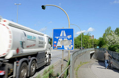 Autobahnauffahrt in Hamburg Stellingen - ein Tanklastzug fährt Richtung Autobahn A7 - ein Mann schiebt sein Fahrrad zur Fussgänger Unterführung unter der Autobahn / Strasse.
