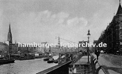 Fassade der Speicherstadt am Kehrwieder - der Zollkanal bildet die Freihafengrenze. Im Binnenhafen liegen Schuten beladen mit Kohle; ein Kahn wird mit einem Schlepper auf dem Kanal gezogen. Die Kirchtürme von der St. Nikolaikirche und der St. Kat