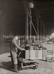 Holztonnen werden in einer Verladekiste vom Schiff an Land gebracht und dort auf eine Dreirad-Transportkarre gestellt. Damit bringt der Hafenarbeiter die Fässer an ihren Lagerplatz; ca. 1930.