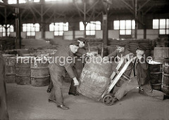 Von Hand setzen die Lagerarbeiter ein schweres Holzfass auf eine Transportkarre. Im Lagerraum des Hamburger Kaischuppens sind Tonnen und Säcke gelagert. ( ca. 1930 )
