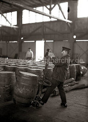 Ein Arbeiter setzt eine Holztonne auf die Selbstladekarre; mit Hilfe eines Eisenhakens wird das Fass auf die Sackkarre gezogen; ca. 1930.