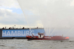 Feuerwehrlöschboot OBERBAURAT SCHMIDT - Wasserfontänen; Schriftzug Hamburg an der Wand vom Schwimmdock.