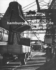 Kohlekai am Altonaer Hafen; Kräne schütten die Kohle in die bereitstehenden Lastwagen -  Hafenarbeiter dirigieren das Schüttgut mit einer langen Stange - im Hintergrund ein Güterwaggon auf den Schienen der Hamburger Hafenbahn. (ca. 1935)
