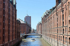 Fleet mit historischen hohen Speichergebäuden in der Speicherstadt Hamburg - unter den Kupferdächern sind Winden angebracht, die früher die Last von Schuten in die Lagerräume gehievt haben. Eine Barkasse fährt mit Touristen auf dem Brooksfleet - im H