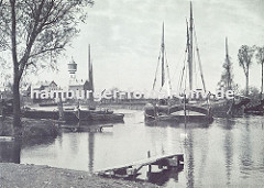 historisches Motiv vom Finkenwerder Fischereihafen - Fischerboote liegen vor Anker, ein Bootssteg führt ins Wasser. Im Hintergrund der Finkenwerder Wasserturm und Werftgebäude