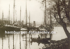 mehrere Fischkutter liegen bei den Landungsbrücken von Hamburg Finkenwerder - ein Ruderboot mit zwei Jungen an Bord liegt am Ufer. Im Hintergrund ein weiteres Ruderboot mit Kindern.