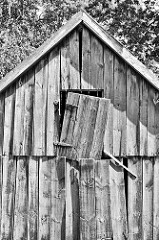 Alte Holzscheune, die Bretter und Tür hängen schief an der Fassade - Schwarz Weiss Bild.