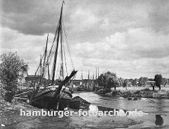 das Köhlfleet in Hamburg Finkenwerder bei Ebbe - das Fleet ist fast trocken und die Frachtschiffe, Fischkutter und Schuten liegen fest im Schlick; am gegen über liegenden Ufer stehen Weiden an der Wiese.