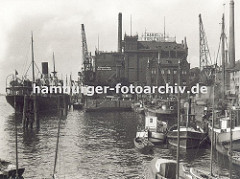 Blick auf den grossen Kohlespeicher am Hafen von Hamburg - Altona; grössere Schiffe und kleine Boote liegen am Kai oder den Dalben; im Vordergrund zwei Sport-Segelboote. (ca. 1935)