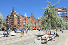 Dar-es-Salaam Platz am Magdeburger Hafen in der Hafencity Hamburgs - Touristen sitzen in der Sonne auf Bänken unter Olivenbäumen.