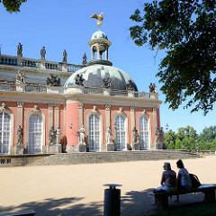 Seitengebäude des Neuen Palais in Potsdam, Park Sanssouci - Parkbank im Schatten unter Bäumen.