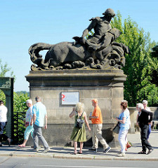 Dekorelement - Figur auf dem Brückenpfosten an der Berliner Seite der Glienicker Brücke; Tafel  zur Geschichte der Brücke auf der Berliner Seite; Touristen gehen vorbei.