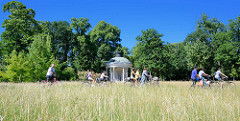 Fahrradfahrer auf dem Fahrradweg durch den Park Sanssouci, hohes Gras auf der Wiese vor dem Pavillon  Park Sanssouci in Potsdam - der Freundschaftstempel ist ein kleiner Rundtempel, den der preußische König Friedrich II. zum Andenken an seine 1758 ve
