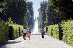 Blick durch die Hauptallee vom Potsdamer Park Sanssouci - SpaziergängerInnen zwischen Buchenhecken; im Hintergrund Springgbrunnen und Kuppel vom Neuen Palais.