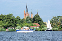 Blick vom Wasser über die Havel zur Heiligen Geist Kirche der Stadt Werder; ein Segelboot fährt auf dem Fluss.