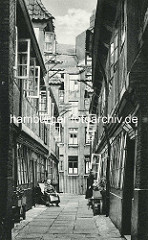 Historische Bilder aus dem Hamburger Gängeviertel - Krameramtswohnungen im Krayenkamp - die Fenster sind geöffnet - eine Frau sitzt mit einer Zeitung im Stuhl - eine weitere steht in der geöffneten Tür.