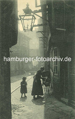 Historische Bilder aus dem Hamburger Gängeviertel - schmaler Gang bei der Steinstrasse; Mutter mit Kind und Kinderwagen - Gaslaterne an der Hauswand, Holzgestelle zum Wäschetrocknen vor den Fenstern.