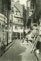 Historische Bilder aus dem Hamburger Gängeviertel - Kinder spielen auf dem Kopfsteinpflaster - eine Frau steht auf der Leiter und putzt Fenster - ein Fahrrad lehnt an der Hauswand einer Kneipe / Bavaria Bier Werbung.