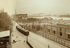 Historische Ansicht der Großen Elbstraße in Altona - geschlossene Güterwaggons stehen auf den Gleisen der Hafenbahn - die Lagerschuppen sind mit einem hohen Zaun gesichert. Im Hintergrund die Elbe und Helgen der Hamburger Werften.grosse-elbstrass