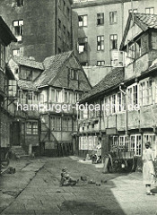 Alte Fotos aus dem Gängeviertel Hamburgs - Kinder spielen auf dem Hof im Schulgang; eine Mutter lehnt in der Tür und schaut zu; Transportkarre.