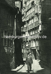 Alte Fotos aus dem Gängeviertel Hamburgs -  Mann mit Anzug und Weste, Schirmmütze im Kornträgergang; Schild Gasthaus, Logierhaus.