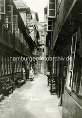 Historische Bilder aus dem Hamburger Gängeviertel - Krameramtswohnungen in Krayenkamp - Bänke mit Blumen / Pflanzen drei Frauen stehen vor der Tür.