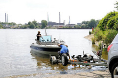 Ein Sportboot wird von einem Trailer auf der Slipanlage im Elbpark Entenwerder zu Wasser gelassen - auf der anderen Seite der Norderelbe Industrieschornsteine und Gebäude auf der Peute in Hamburg Veddel.