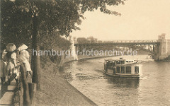 Historisches Motiv der Hamburger Alster - Alsterdampfer und Hochbahnbrücke in Hamburg Winterhude; Frauen mit Hüten stehen am Zaun beim Anleger Winterhuder Fährhaus.