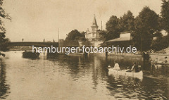 Historisches Foto vom Anleger Winterhuder Fährhaus mit Wartehäuschen aus Holz und Alsterdampfer und Kanu - im Hintergrund das Winterhuder Fährhaus.