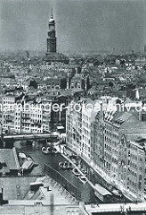 Historischer Blick über das Nikolaifleet der Altstadt Hamburgs - im Vordergrund die Reimersbrücke, in der Bildmitte die Holzbrücke. Barkassen und Arbeitsschiffe liegen an einem Steg - im Hinterrund ragt der Kirchturm der St. Michaeliskirche auf.