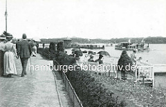 Historisches Motiv vom Alsterufer der Hamburger Binnenalster bei der Rabenstrasse - Spaziergänger, Frau mit Feder am Hut - Mann, Herr mit Melone und Spazierstock - ein Alsterdampfer fährt zum Anleger.