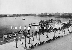 Historische Ansicht vom Alsterpavillion an der Hamburger Binnenalster - Pferdedroschken warten am Strassenrand - Ruederboote am Bootssteg; Alsterdampfer fahren zum Anleger.