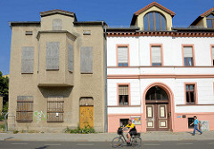 Alt + neu; Wohnhaus mit Rauhputzfassade und zugenagelten Fenstern - daneben ein restauriertes Gründerzeitgebäude mit farblich abgesetzter Fassade.
