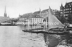 Hamburger Binnenalster am Jungfernstieg - Bootsverleih mit Ruderbooten und Segelboot unter Segeln. Gebäude vom Alsterpavillion und Geschäftshäuser am Jungfernstieg - lks. der Kirchturm der St. Petrikirche.