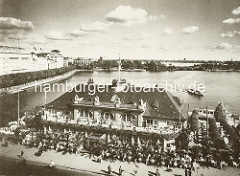 Luftaufnahme vom Alsterpavillion am Jungfernstieg an der Hamburger Binnenalster - ein Alsterdampfer fährt zum Anleger. Die Gäste vom Alsterpavillion sitzen an Tischen im Freien am Jungfernstieg.