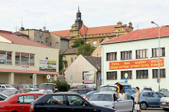 Parkplatz mit Autos vor Geschäften - im Hintergrund das Koliner Schloss mit Kupferturm.