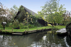 Traditionelles, typisches Holzwohnhaus mit Bootsanlegestelle in Lübbenau - Postkasten am Wasser, ein Hundliegt auf der Wiese und passt auf.