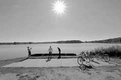 Pause von Fahrradfahrern am See auf der Fahrradroute von Lübben nach Schlepzig - Schwarz-Weiß Fotografie, Gegenlichaufnahme.