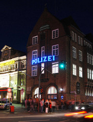 Nachtaufnahme der Backsteinarchitektur von der Davidwache am Spielbudenplatz / Davidstrasse - erleuchteter Schriftzug Polizei; lks. daneben das St. Pauli Theater - Fussgänger warten an der Ampel.