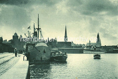 Historisches Panorama vom Lübecker Hafen; ein Küstenschiff liegt am Kai, ein Binnenschiff hat längsseits festgemacht - im Hintergrund die Kirchtürme der Marienkirche und in der Bildmitte der Kirchturm der St. Jacobikirche - lks. der Turm vom Burgt