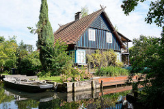 Wohnhaus im Grünen am Wasser - Gebäude mit farbig abgesetzter Holzfassade - Kahn mit Sitzbänken am Ufer.