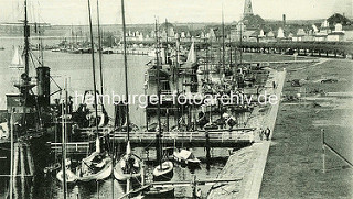 Historische Aufnahme vom Hafen in Travemünde - Segelboot und Dampfer am Steg; im Hintergrund die Strandpormenade und der Kirchturm der St. Lorenz Kirche.