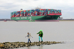 Kinder spielen auf einer Steinbuhne am Elbufer - auf der Elbe der havarierte, aufgelaufene Containerfrachter CSCL Indian Ocean.