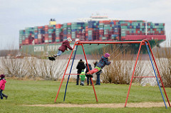 Kinderspielplatz in Grünendeich an der Elbe - Kinder auf der Schaukel; im Hintergrund das havarierte Containerschiff CSCL Indian Ocean.